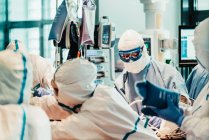 Gruppo di medici professionisti che indossano maschere protettive e tute in piedi vicino al tavolo operatorio con attrezzature e si preparano per l'operazione nella moderna clinica — Foto stock