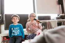 Ragazza in occhiali cantare canzone karaoke mentre seduto vicino al fratello in camera accogliente il giorno del fine settimana a casa — Foto stock
