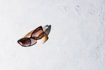 De dessus les lunettes de soleil à la mode avec coquillage placé sur la surface rugueuse de stuc par une journée ensoleillée pendant les vacances d'été — Photo de stock