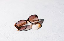 Dall'alto occhiali da sole alla moda con conchiglia posta sulla superficie ruvida di stucco nella giornata di sole durante le vacanze estive — Foto stock