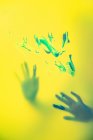 Crop craftswoman with painted hands standing behind translucent yellow wall with brushstrokes — Stock Photo