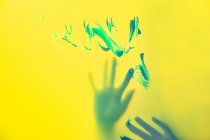 Crop craftswoman with painted hands standing behind translucent yellow wall with brushstrokes — Stock Photo