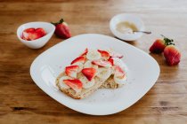 Délicieux sandwichs à la banane et à la fraise avec purée sucrée placée sur une assiette pendant le petit déjeuner sur une table en bois — Photo de stock