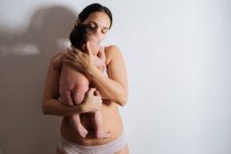 Feliz jovem mãe no sutiã segurando bonito pequeno bebê em mãos no branco sala de luz — Fotografia de Stock