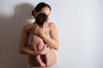 Felice giovane madre in reggiseno che tiene carino piccolo bambino sulle mani nella stanza luce bianca — Foto stock
