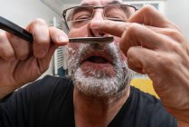 Hombre barbudo afeitándose con navaja de afeitar recta - foto de stock