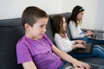 Grupo de crianças usando laptops enquanto se senta no sofá em casa — Fotografia de Stock