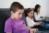 Gruppe von Kindern benutzt Laptops, während sie zu Hause auf dem Sofa sitzen — Stockfoto