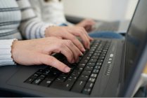 Side view of anonymous woman in casual clothes typing on laptop keyboard while working on freelance work at home — Stock Photo