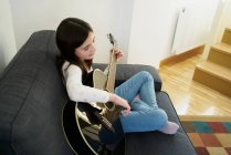 Jovem aprendendo irmã a tocar guitarra no sofá em casa — Fotografia de Stock
