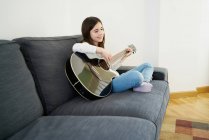 Jovencita aprendiendo hermana a tocar la guitarra en el sofá en casa - foto de stock
