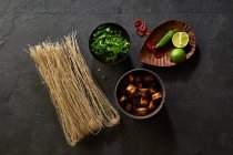 Ingredientes para cocinar ramen vegetariano con tofu colocado en el fondo oscuro - foto de stock