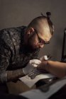 Татуировщик с помощью машины и сделать татуировку с черными чернилами в салоне в анонимном обрезанном клиенте — стоковое фото