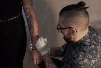 Alto angolo di tatuaggio maschile che fa tatuaggio a mano libera e schizzo di disegno sul braccio del cliente del raccolto nel salone — Foto stock
