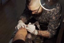 Зверху татуїст використовує машину і робить татуювання з чорним чорнилом в салоні в анонімному обрізаному клієнті — стокове фото