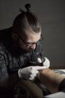 Tatoueur utilisant la machine et la fabrication de tatouage à l'encre noire dans le salon dans un client recadré anonyme — Photo de stock