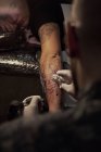 Desde arriba de tatuador masculino irreconocible usando la máquina y haciendo tatuaje en el brazo del cliente de la cosecha en el salón - foto de stock