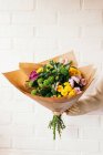 Arm with bunch of fresh colorful flowers on background of the white brick wall — Stock Photo
