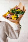 Ernte unkenntliche Person, die mit einem Strauß frischer bunter Blumen auf dem Hintergrund der weißen Ziegelwand steht — Stockfoto