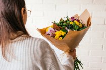 Crop unrecognizable person standing with bunch of fresh colorful flowers on background of white brick wall — Stock Photo