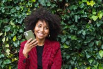 Contenuto Donna afroamericana seduta sulla panchina in città e che parla sullo smartphone guardando altrove — Foto stock
