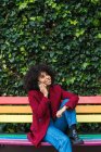Задоволена афроамериканка сидить на лавці в місті і розмовляє на смартфоні, дивлячись у далечінь. — стокове фото