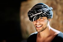 Joven alegre guapo étnico árabe macho con turbante modelo vistiendo hipster ropa de verano con estilo mirando hacia otro lado mientras está de pie en la calle - foto de stock