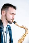 Seitenansicht eines kreativen männlichen Musikers, der Saxofon spielt, während er auf weißem Hintergrund steht und wegschaut — Stockfoto