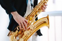 Crop männlicher Musiker spielt Saxofon, während er auf weißem Hintergrund steht und wegschaut — Stockfoto