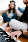 Mann spielt Synthesizer und Frau hört Musik über Kopfhörer, während sie zu Hause auf dem Boden sitzt und neue Songs aufnimmt — Stockfoto