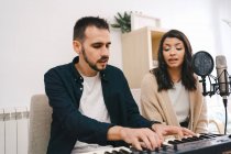 Мужчина-музыкант играет на синтезаторе и поет вместе с женщиной во время записи песни дома — стоковое фото