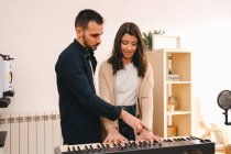 Male musician playing synthesizer and singing together with woman while recording song at home — Stock Photo