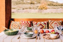 Tisch serviert mit Geschirr und verschiedenen reifen Früchten und köstlichen Häppchen auf der Terrasse — Stockfoto