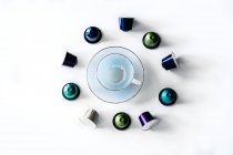 Top view of collection of coffee pods placed near empty ceramic mug and saucer on white background — Stock Photo