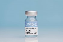 Glasflasche mit Impfstoff von COVID 19 auf Tisch auf blauem Hintergrund — Stockfoto