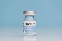 Frasco para injetáveis de vidro com a vacina COVID 19 colocada na mesa sobre fundo azul — Fotografia de Stock