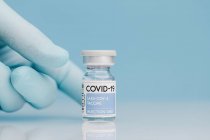 Primo piano del medico non riconoscibile con raccolta del flaconcino di vetro con vaccino di COVID 19 posto sul tavolo su fondo blu — Foto stock