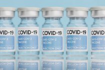 Flaconcini di vetro con vaccino di COVID 19 disposti sul tavolo in fila su fondo blu — Foto stock