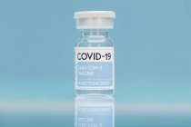 Скляний флакон з вакциною від COVID 19 розміщений на столі на синьому фоні — стокове фото