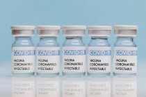 Флаконы со стеклом с вакциной от COVID 19 помещены на стол подряд на синем фоне — стоковое фото