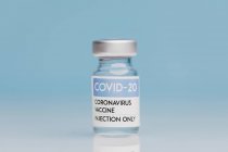 Скляний флакон з вакциною від COVID 19 розміщений на столі на синьому фоні — стокове фото
