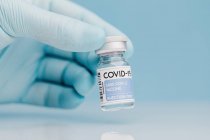 Primo piano del medico non riconoscibile con raccolta del flaconcino di vetro con vaccino di COVID 19 posto sul tavolo su fondo blu — Foto stock