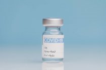Флакон со стеклом с вакциной от COVID 19 помещен на стол на синем фоне — стоковое фото