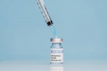 Jeringa médica y vial de vidrio con vacuna contra el coronavirus colocados sobre fondo azul - foto de stock