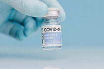 Fechar o fecho do médico irreconhecível com a recolha de frasco de vidro com a vacina COVID 19 colocada na mesa sobre fundo azul — Fotografia de Stock