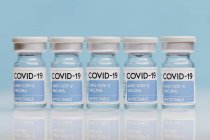 Frascos para injetáveis de vidro com vacina COVID 19 colocados na mesa sobre fundo azul — Fotografia de Stock