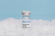 Glasflasche mit Impfstoff von COVID 19 auf Eis in der Tiefkühltruhe auf blauem Hintergrund — Stockfoto