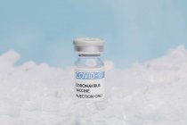 Flacon en verre avec vaccin de COVID 19 placé sur glace au congélateur sur fond bleu — Photo de stock