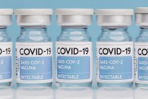 Viales de vidrio con vacuna de COVID 19 colocados en la mesa en fila sobre fondo azul - foto de stock
