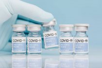 Primer plano del médico irreconocible con la recogida de viales de vidrio con vacuna de COVID 19 colocados en la mesa en fila sobre fondo azul - foto de stock